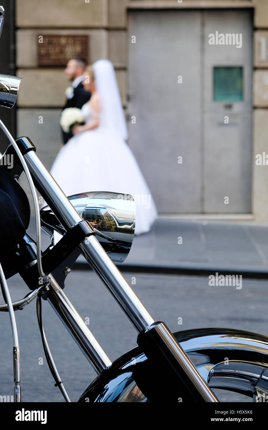 Close up of motorbike wheel parked on Flinders Lane, Melbourne, Victoria, Australia, with bride and groom walking up street Stock Photo
