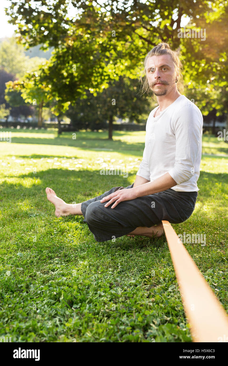 Man sitting on tightrope or slackline concentrating to keep balance