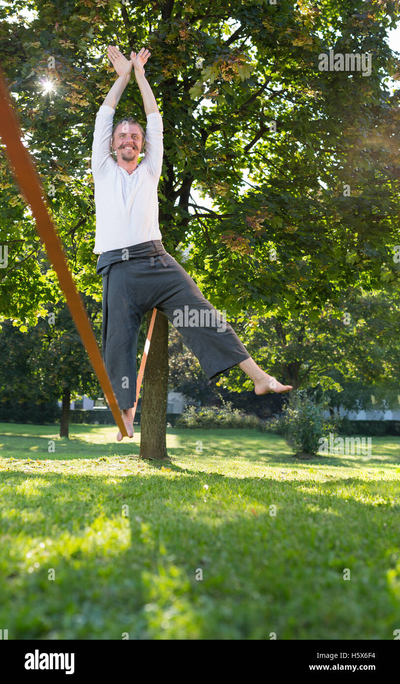 Portrait of handsome young man walking on slackline in the park Stock
