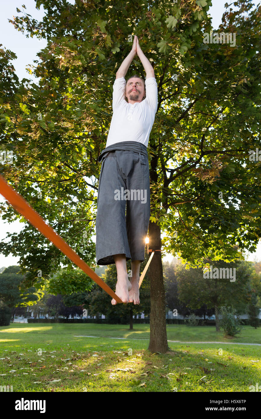 Portrait of handsome young man walking on slackline in the park Stock