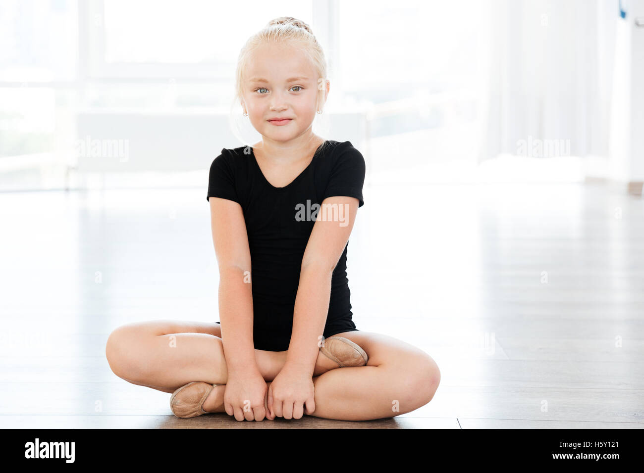 Portrait of happy beautiful little girl ballerina sitting with legs