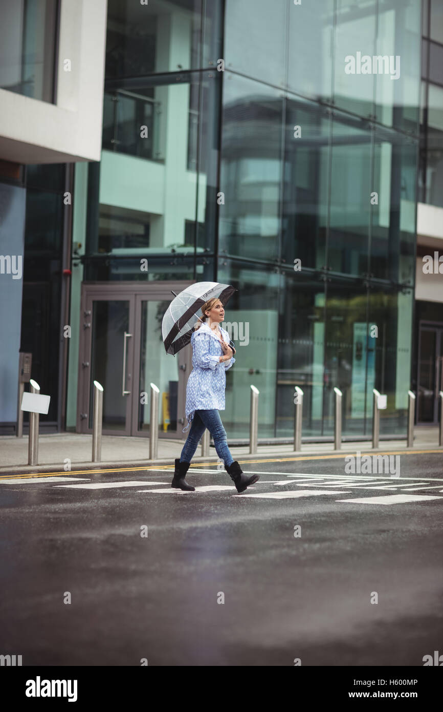 Woman holding umbrella and crossing street Stock Photo