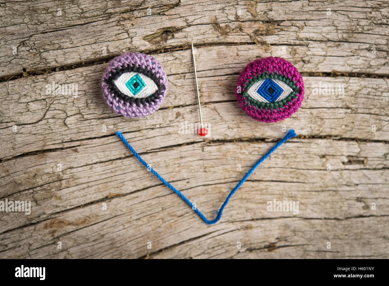 Face, two Posamentenknöpfe as eyes, pin as a nose and yarn as a mouth on wooden panel Stock Photo