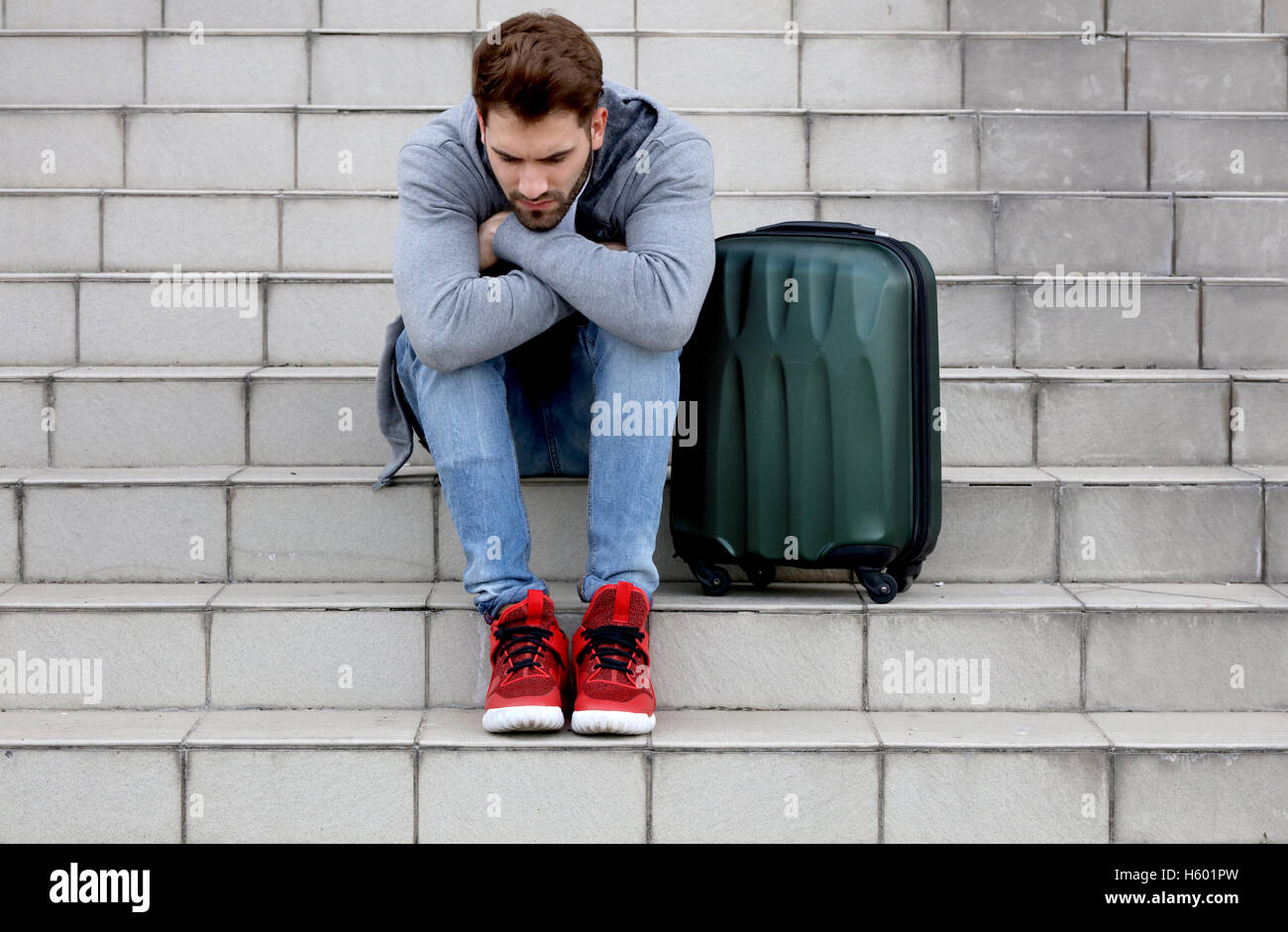 young man sitting on concrete stairs with suitcase Stock Photo
