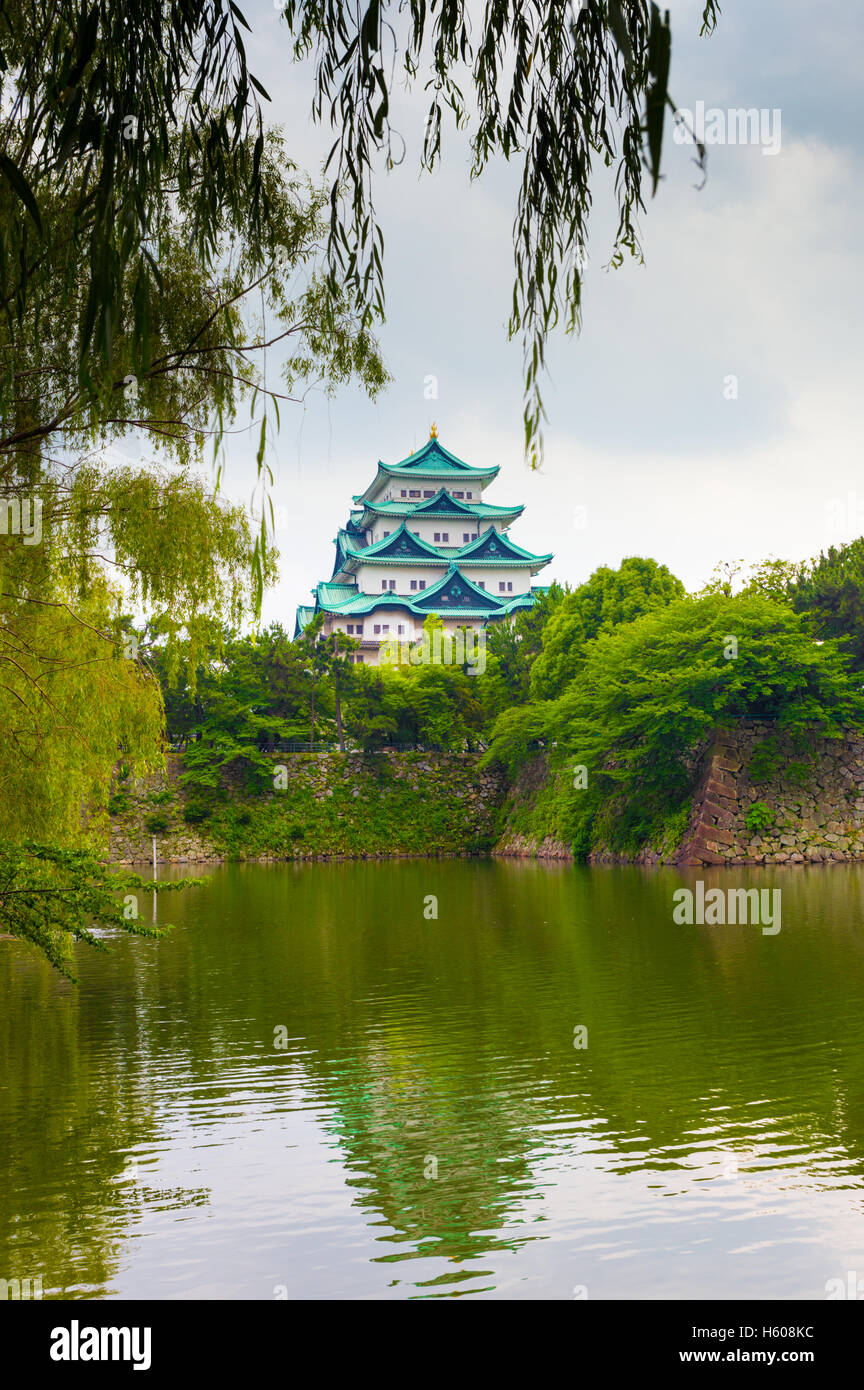 Hanging leaves frame the historic Nagoya Castle stronghold above a watery moat and strong walled rampart in Japan. Vertical Stock Photo