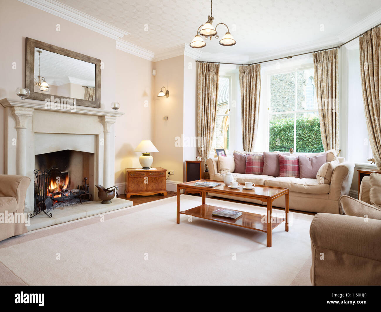 A large traditional, homely Victorian livingroom with an impressive fireplace and roaring fire. UK Stock Photo