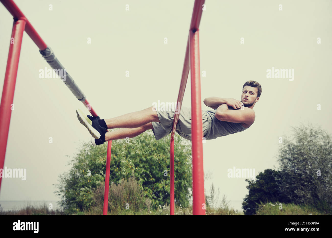young man doing sit up on parallel bars outdoors Stock Photo