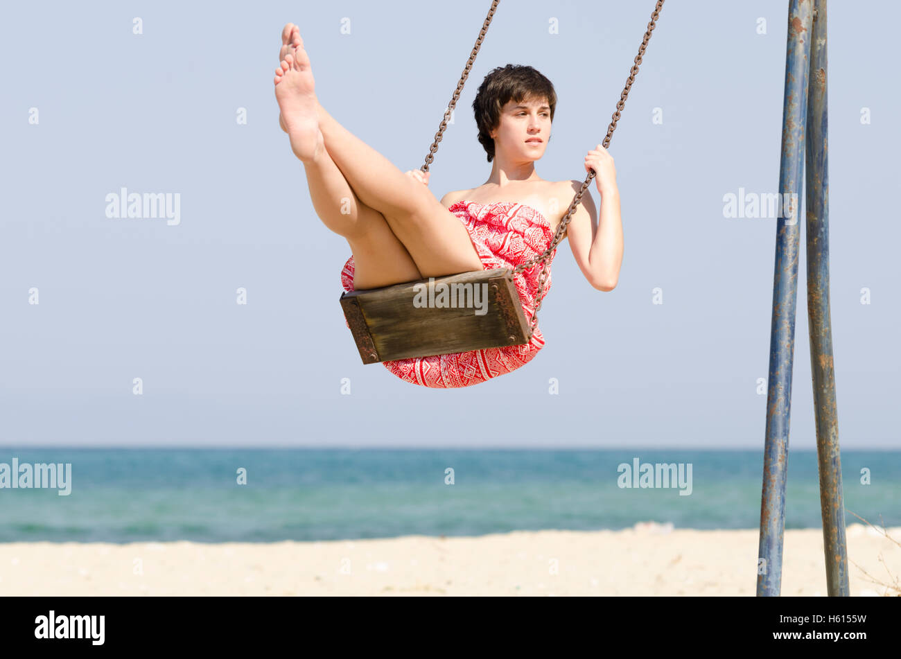 Young woman in a red dress swing by the beach Stock Photo