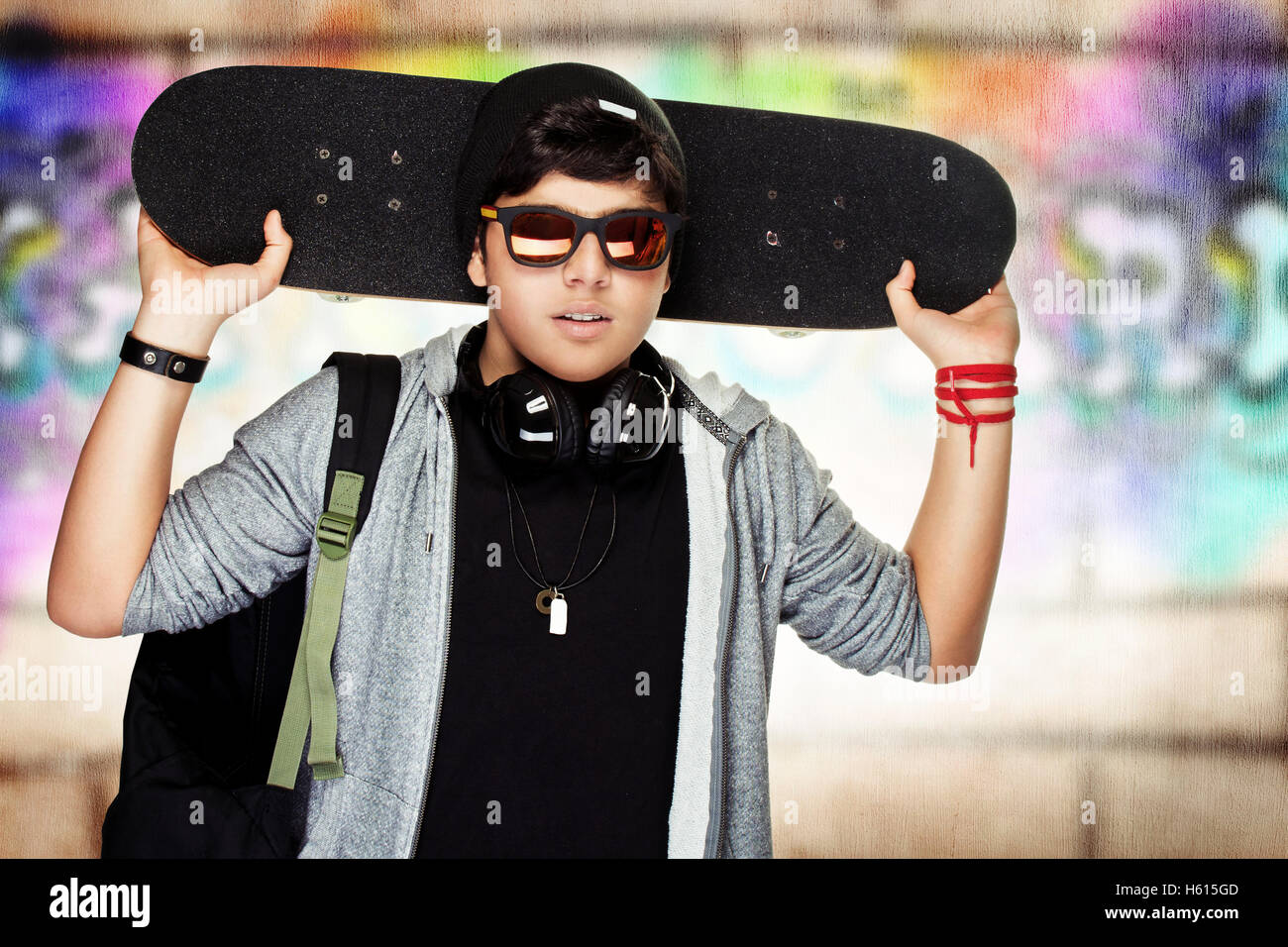 Stylish teen boy with skateboard, urban graffiti wall background, active handsome guy listening music, modern life of youth Stock Photo
