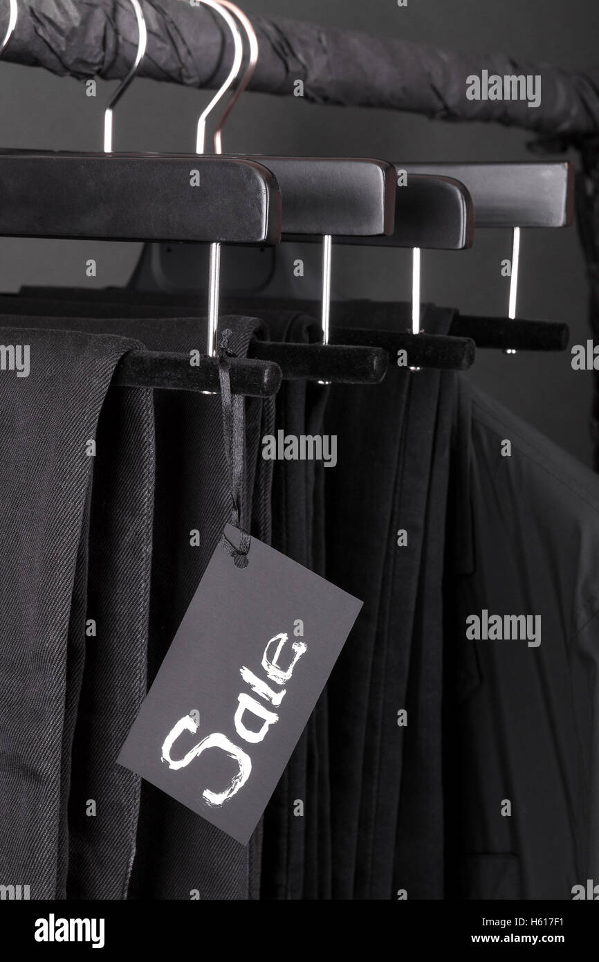A lot of black pants jeans and jacket hanging on clothes rack. Black