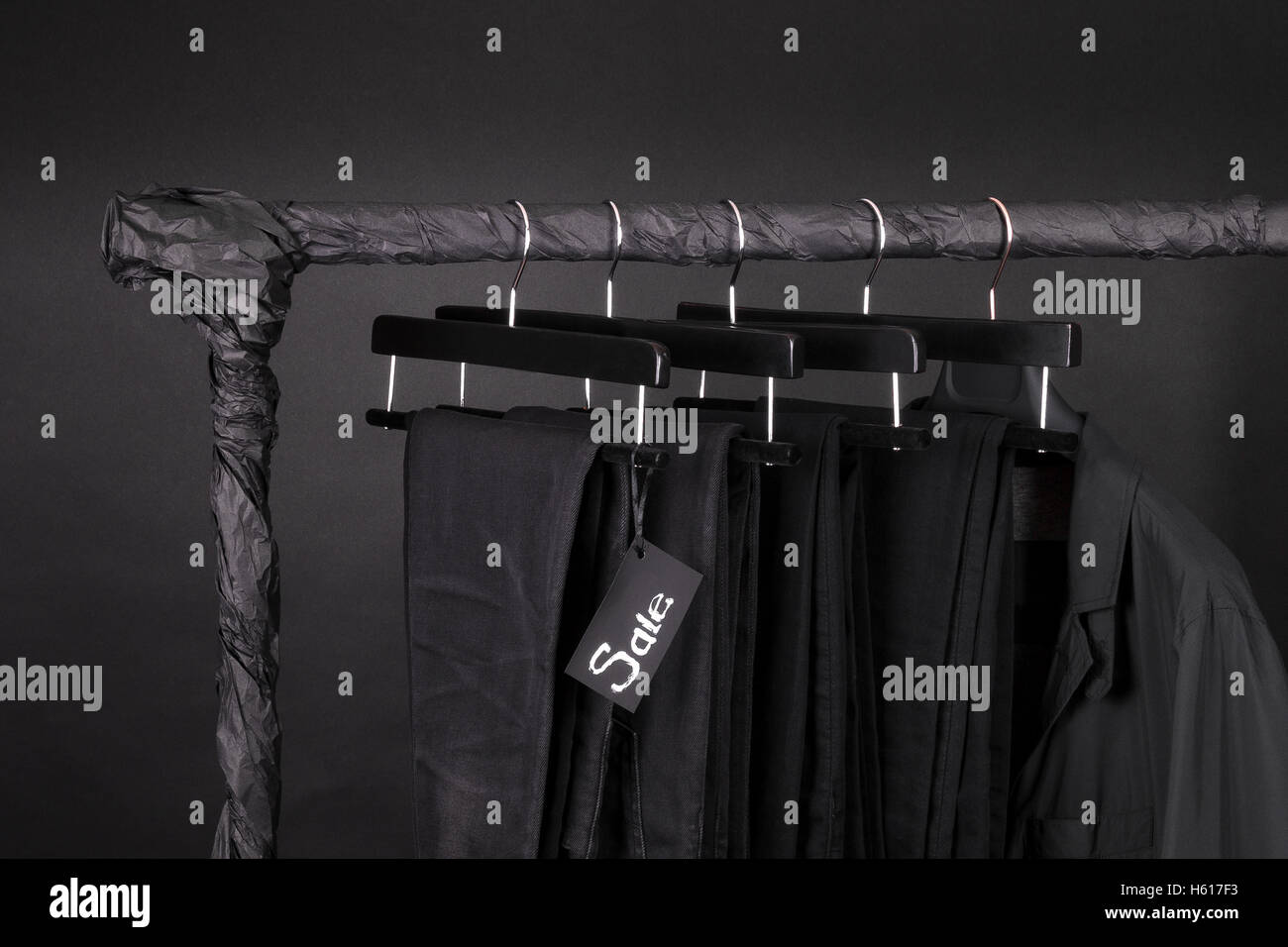 A lot of black pants jeans and jacket hanging on clothes rack. Black