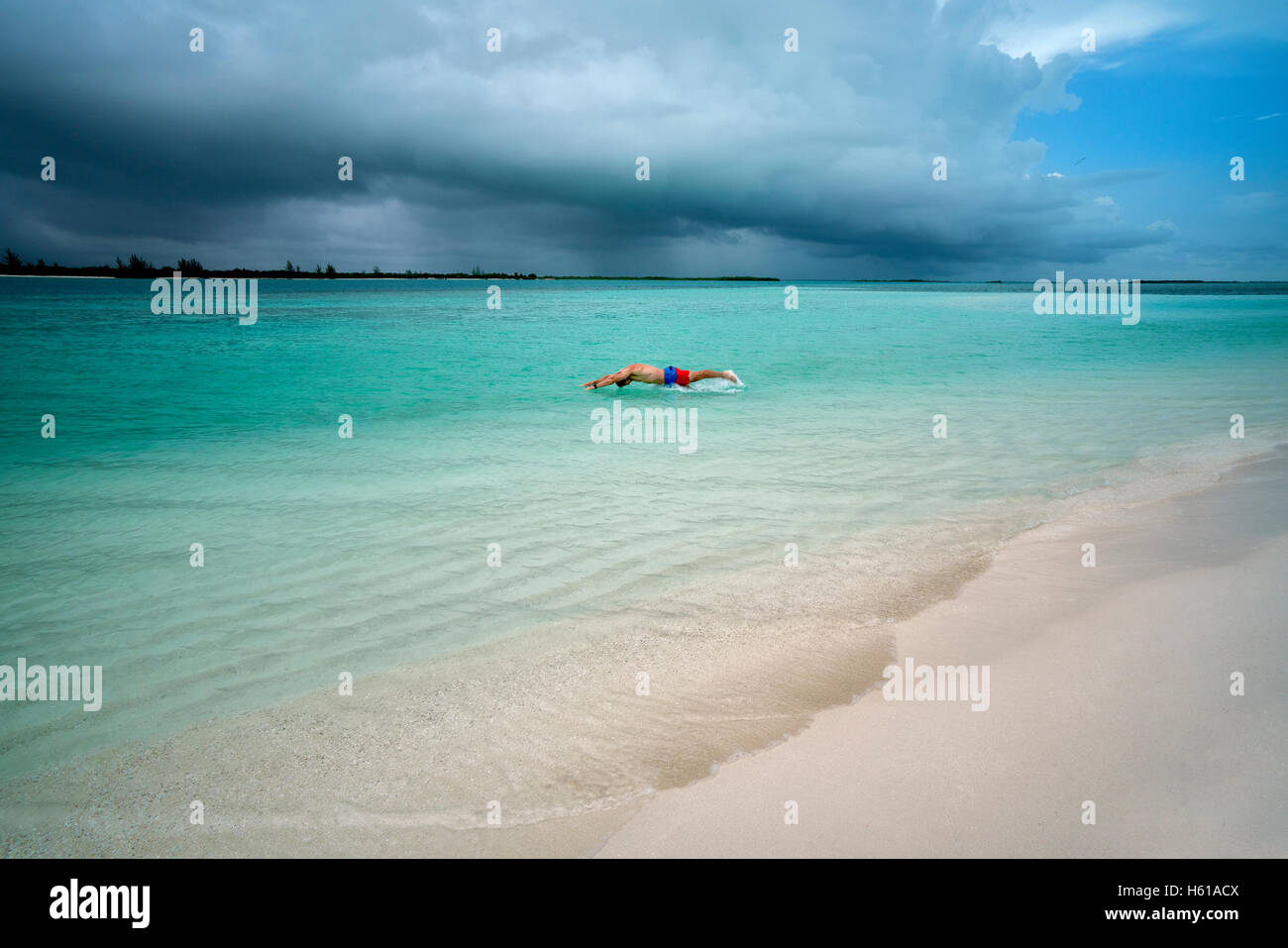 Man diving in water with storm clouds over ocean at Turks and Caicos. Stock Photo