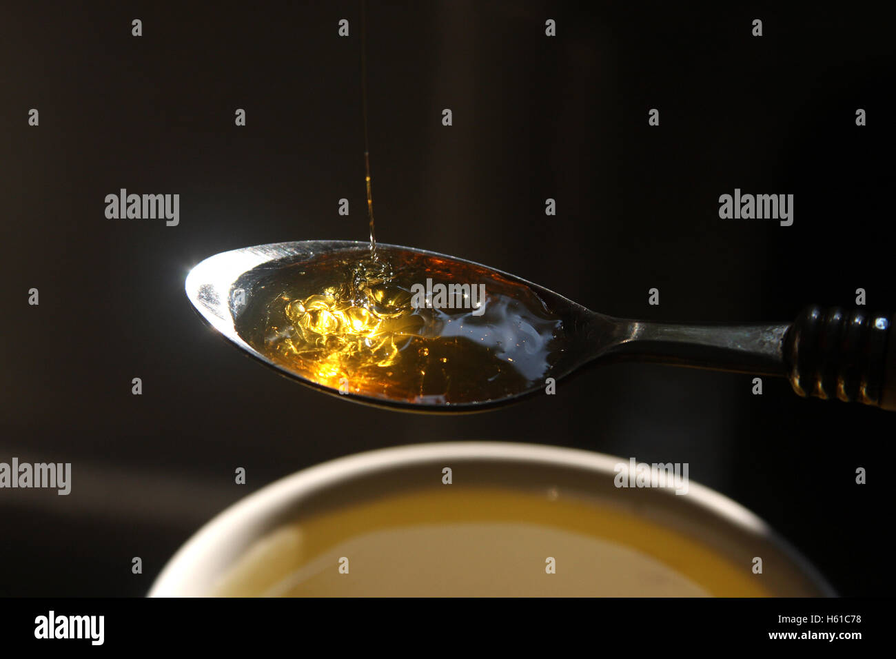 Teaspoon filled with honey poured into cup of tea Stock Photo
