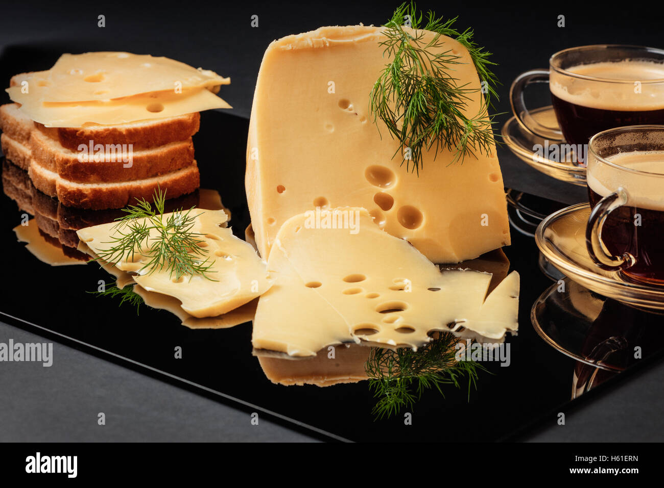 Cheese with fennel, white loaf and two cups of coffee on a black background Stock Photo