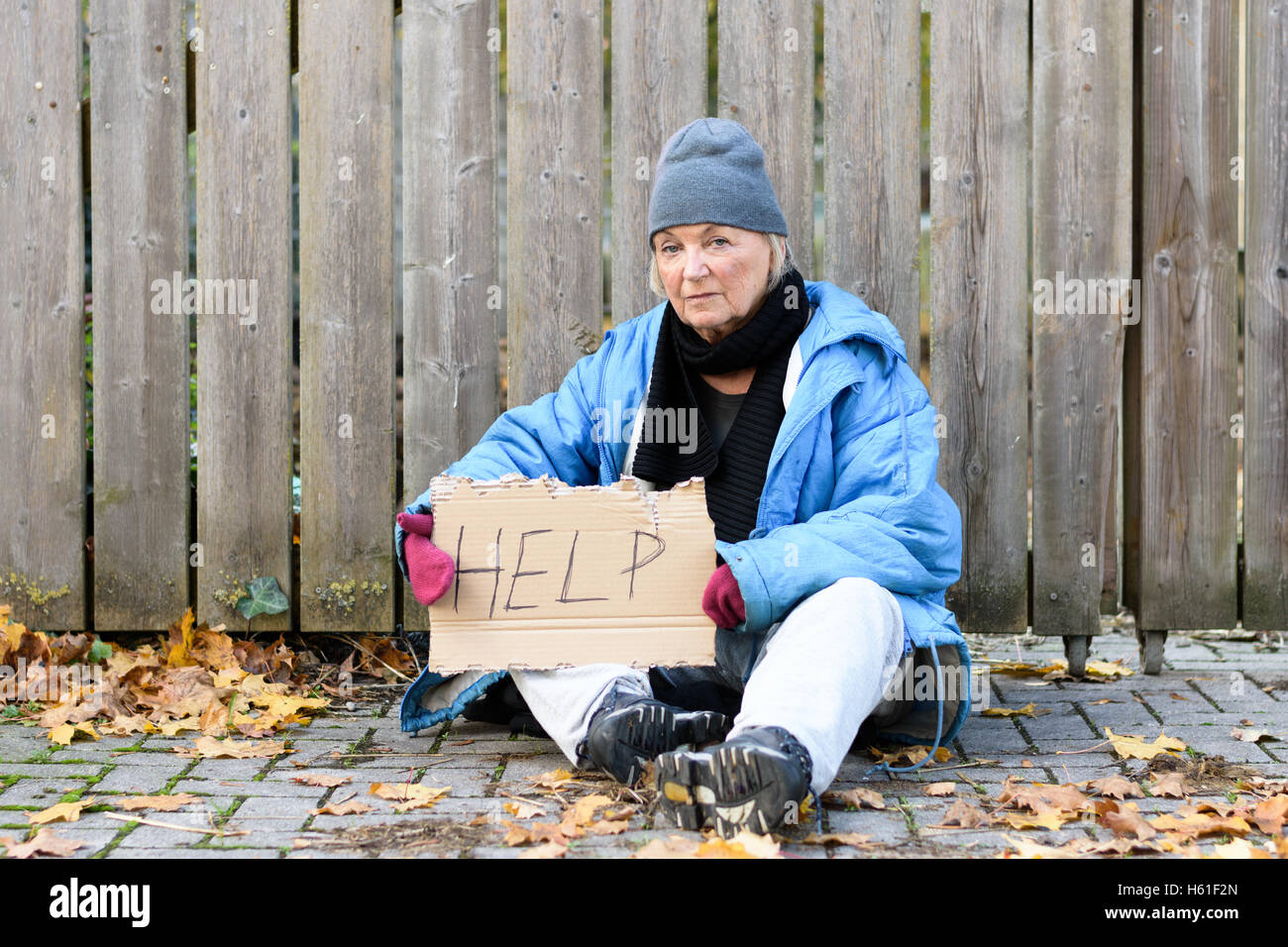 Elderly homeless woman sitting on a cobbled sidewalk with a hand