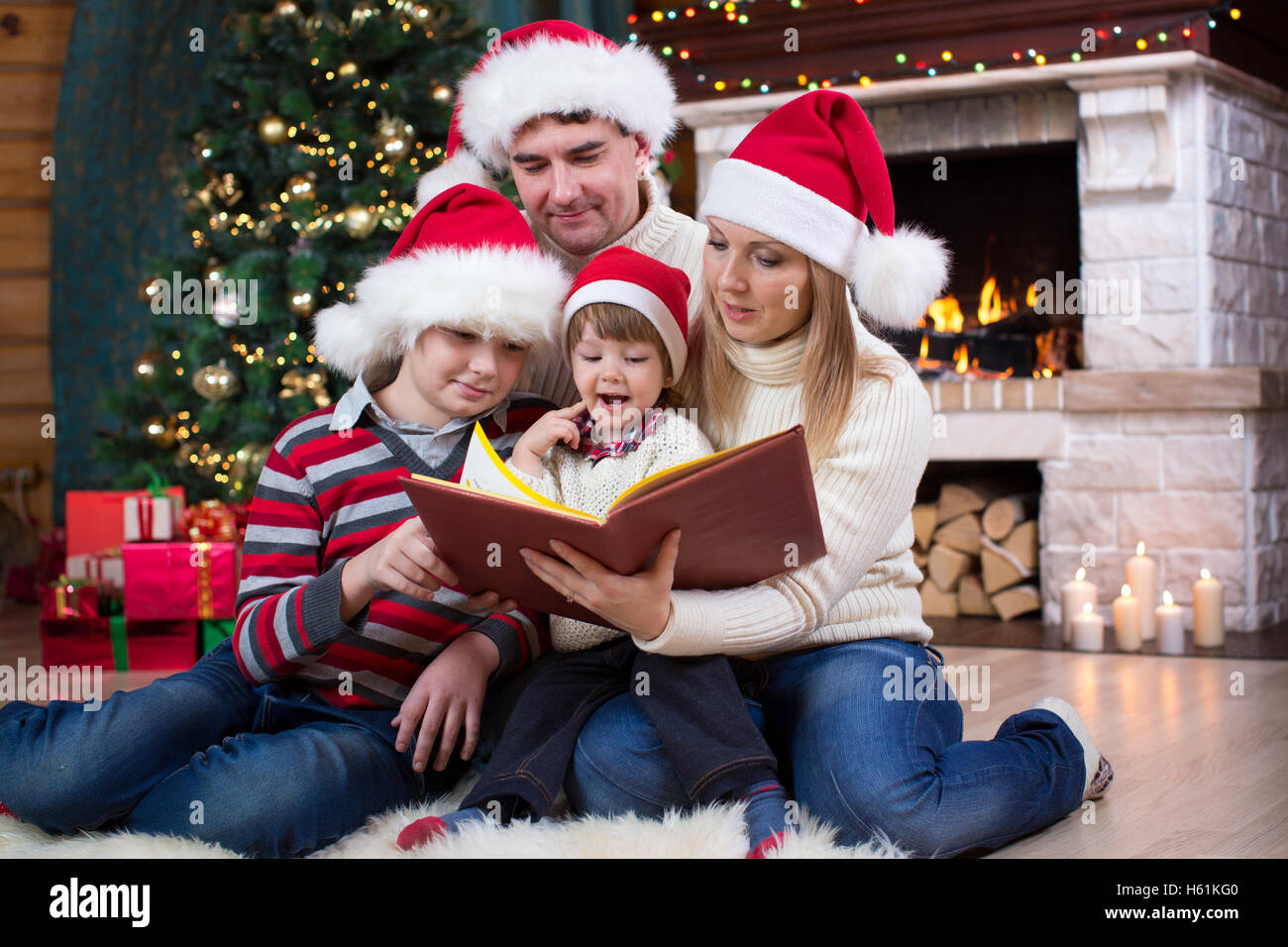 Family read stories sitting on sofa in front of fireplace in Christmas decorated house interior Stock Photo