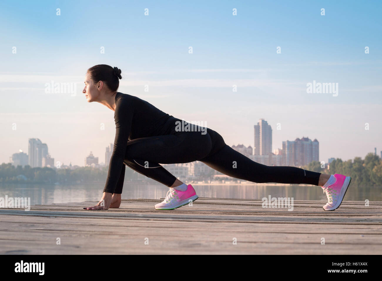 Young pretty fitness woman exercises on pier during morning sport training workout Stock Photo
