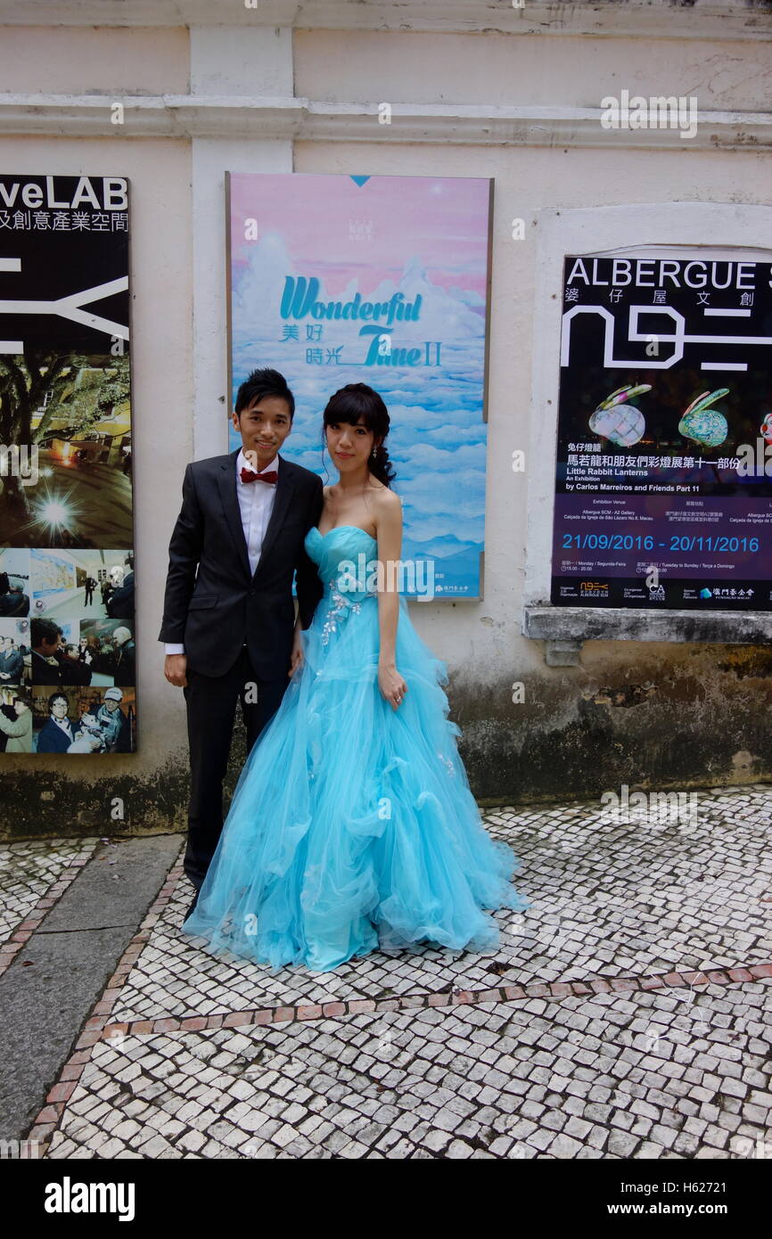 passing couple having wedding photos taken her dress matching the turquoise poster Macau China old town Stock Photo