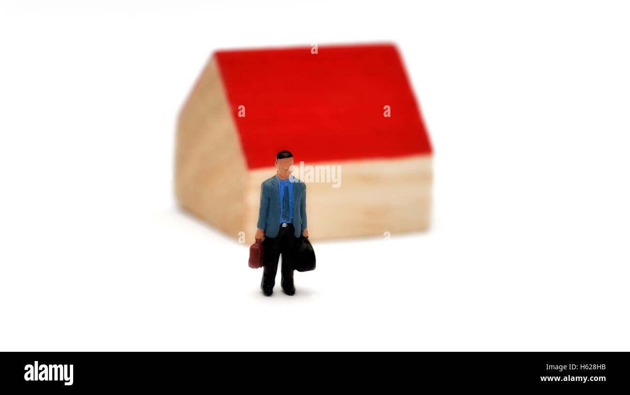 A miniature figurine walking away from a house with red roof. Stock Photo
