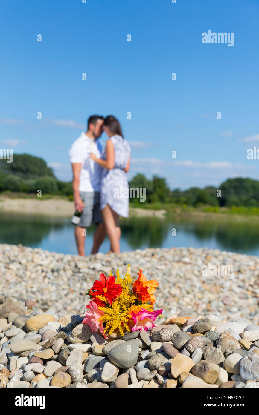 Bunch of flower on pebbles by river, romantic couple standing in background Stock Photo