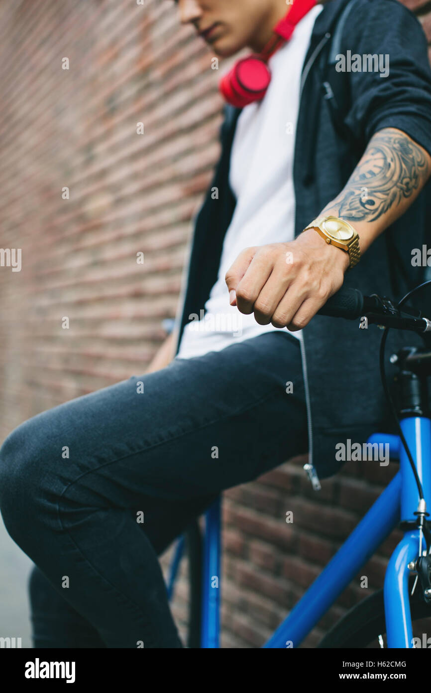 Teenager with a fixie bike, golden clock and tattoo on forearm Stock Photo