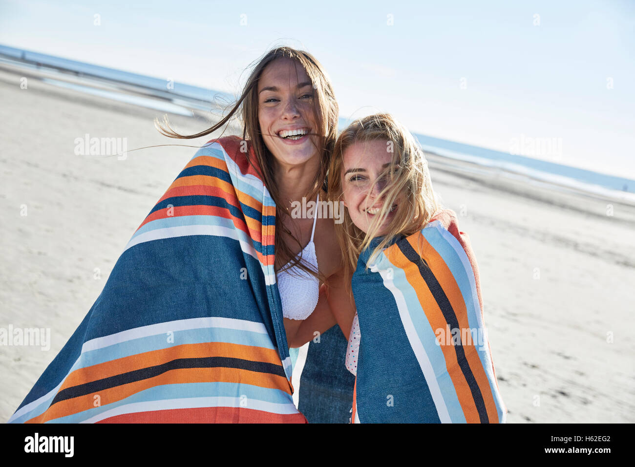 Two happy young women wrapped in a blanket on the beach Stock Photo Alamy