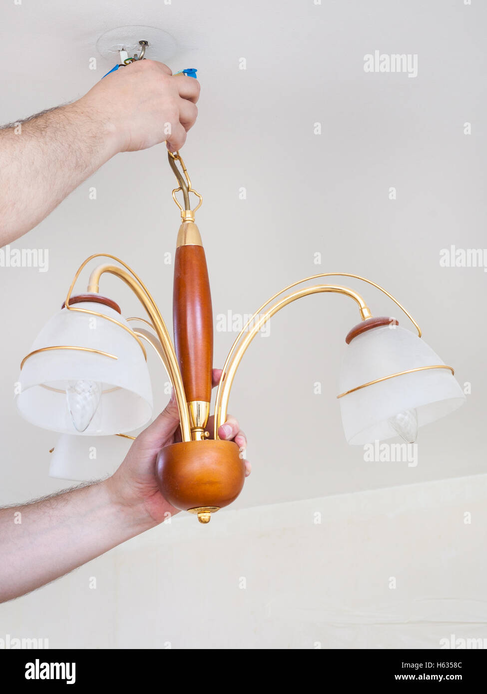 electrician removes ceiling chandelier for repairing in room Stock Photo