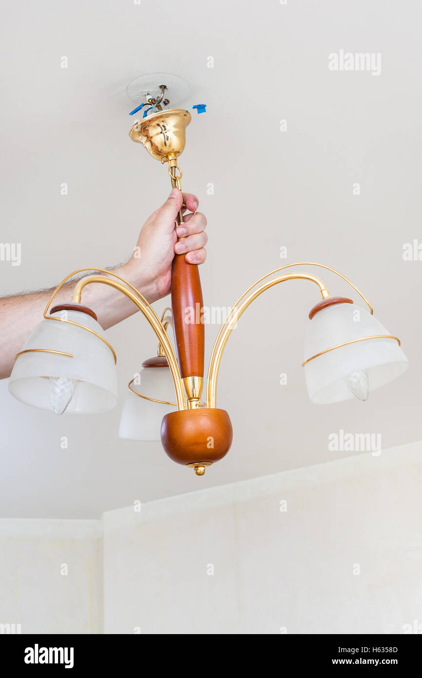 electrician removes hanging ceiling chandelier for repairing in room Stock Photo