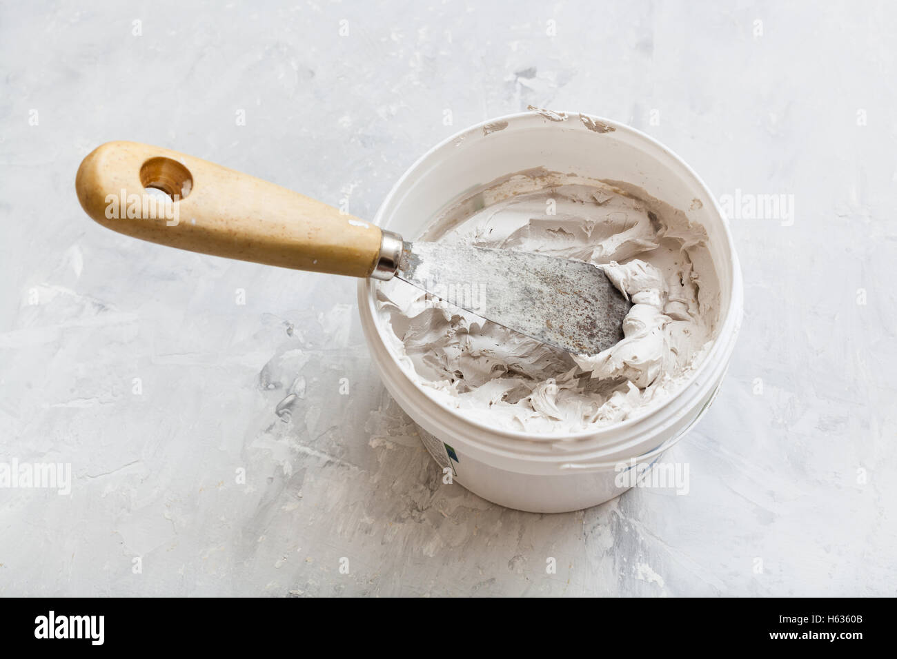 metal spatula with wooden handle in tube with putty on the concrete floor Stock Photo
