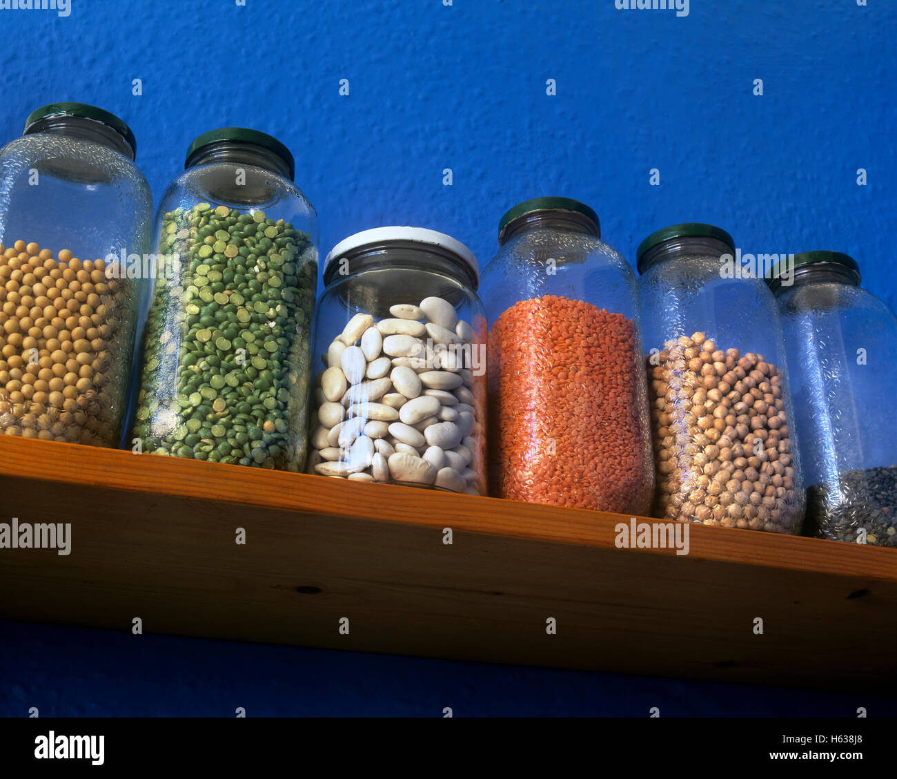 Pulses in storage jars on a kitchen shelf: soya beans, green split peas, butter beans, red lentils, chick peas, puy lentils. Stock Photo