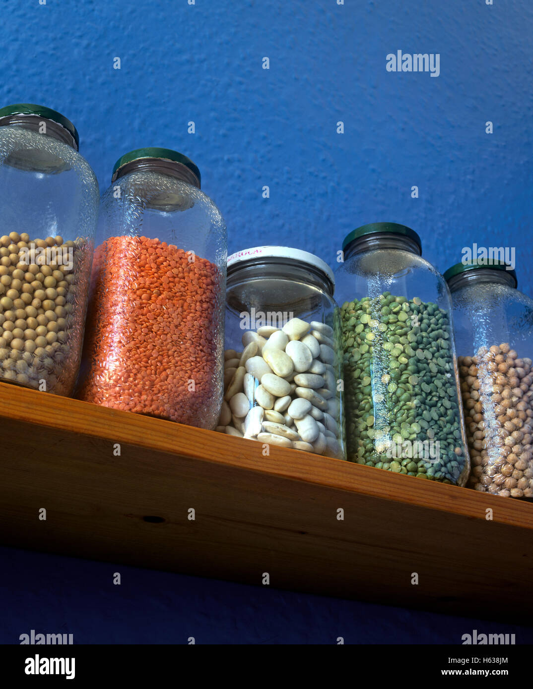 Pulses in storage jars on a kitchen shelf. From left: soya beans, red lentils, butter beans, green split peas, chick peas. Stock Photo