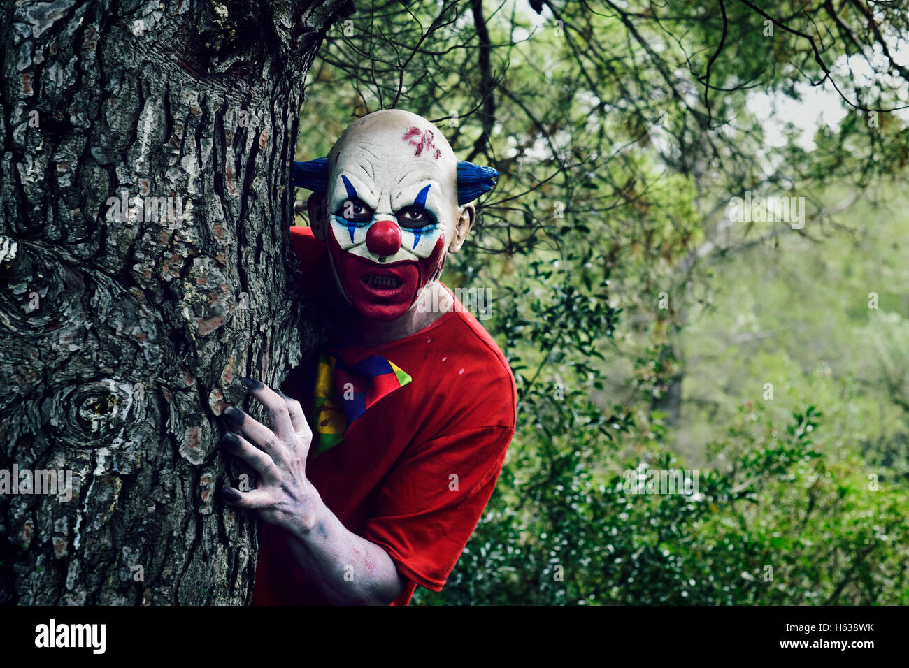 closeup of a scary evil clown in the woods, emerging from behind of a