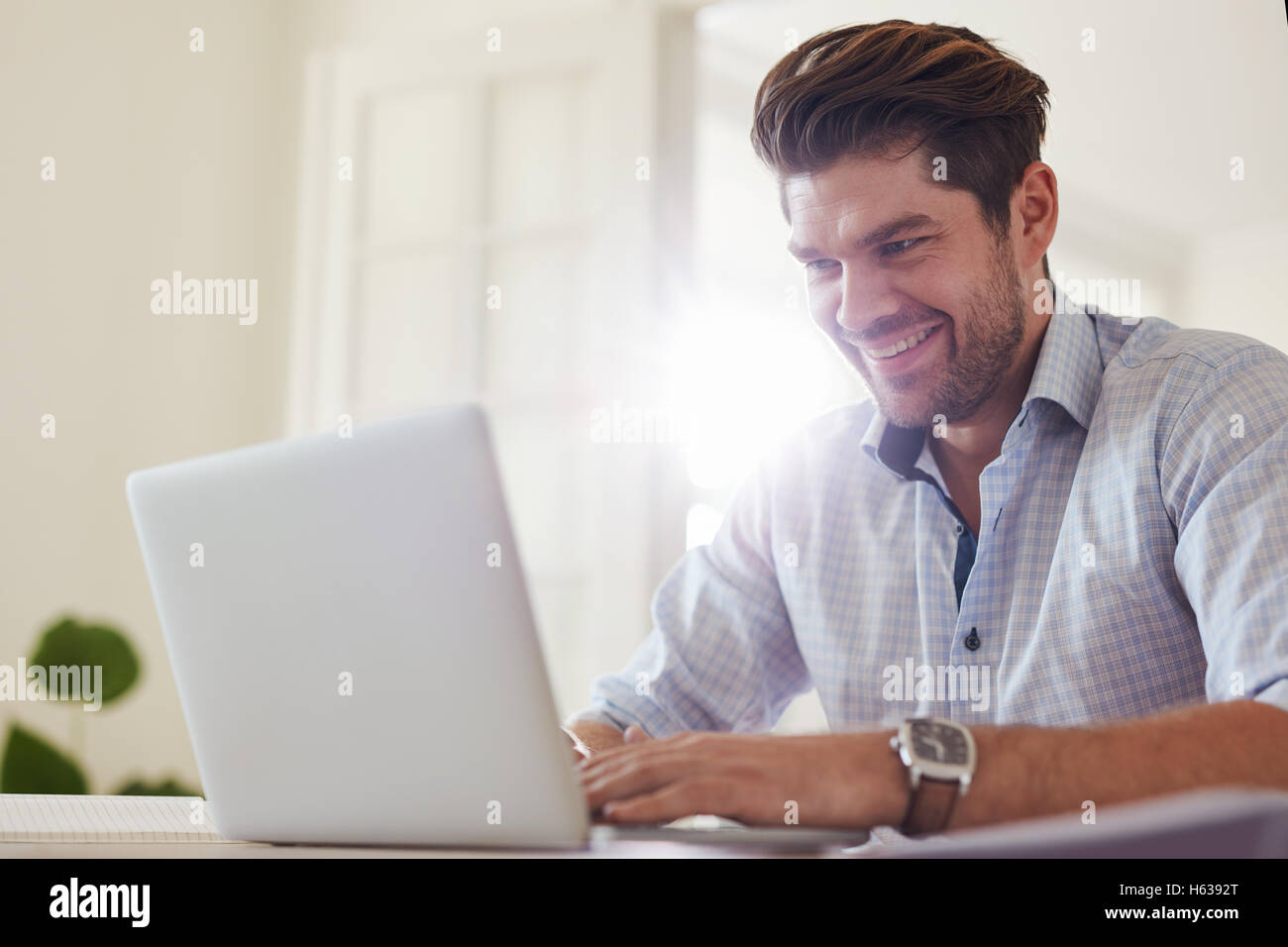 Shot of happy young man sitting at table and working on laptop computer. Businessman working from home office. Stock Photo