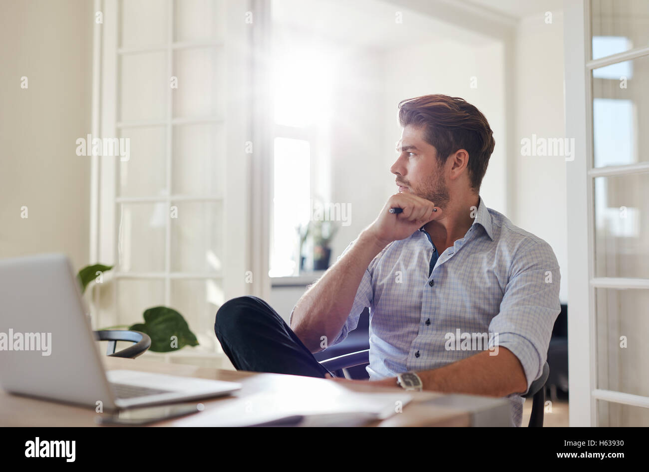 Shot of young man sitting at table looking away and thinking. Thoughtful businessman sitting home office. Stock Photo