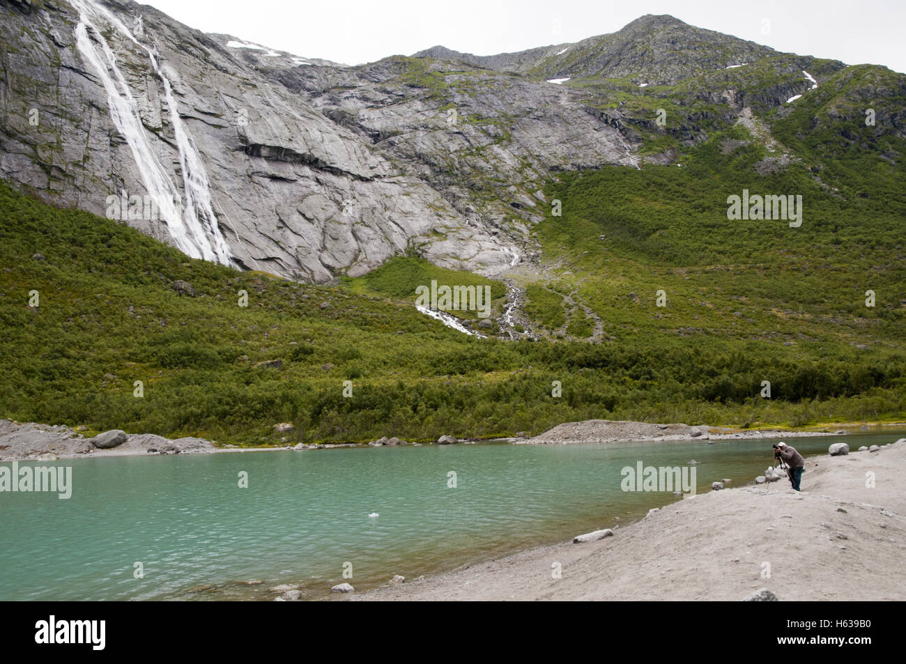 Man taking photos of Briksdal glacier with Tjøtafossen waterfall and the meltwater lagoon, Briksdalen valley, Jostedalsbreen national park, Norway. Stock Photo