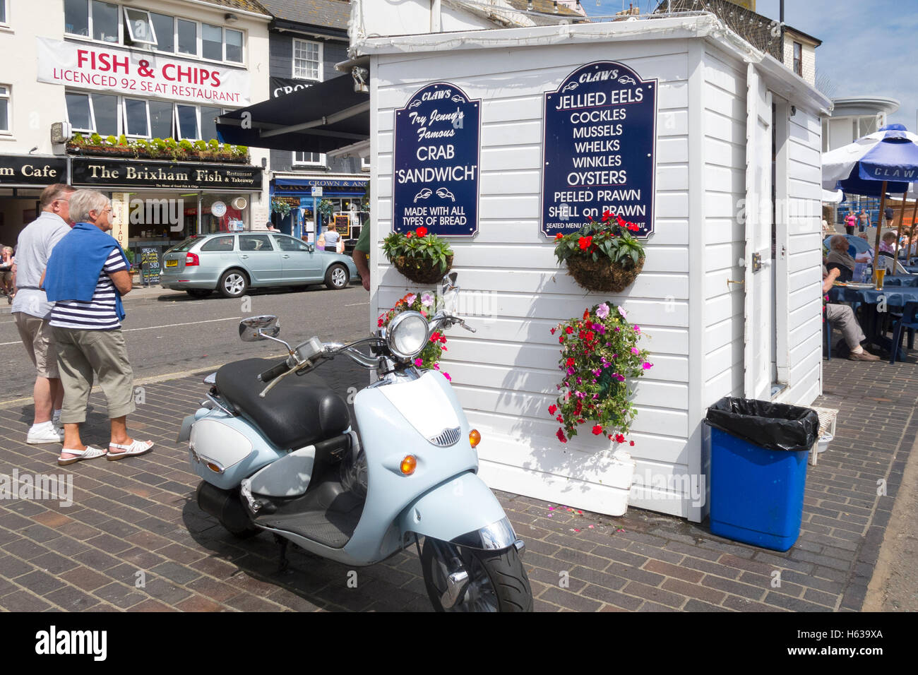 Smart scooter parked outside seafood kiosk at Brixham's busy harbourside in Devon with tourists walking by. Stock Photo