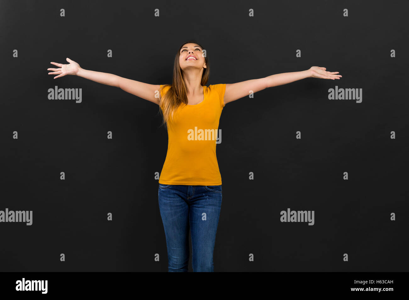 Beautiful woman with arms open in front of a black wall Stock Photo
