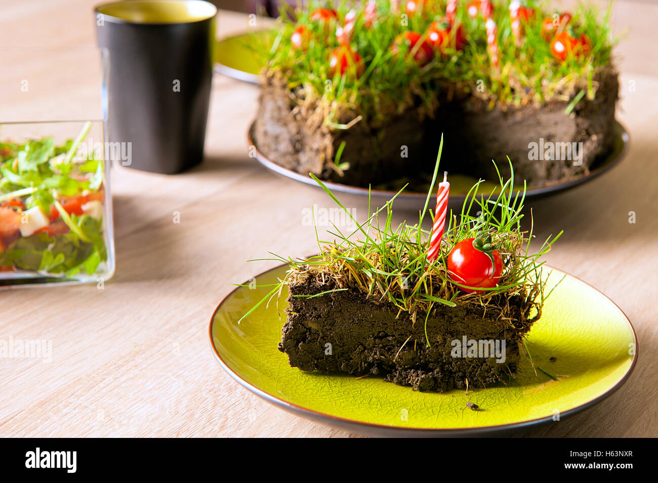 An improvised garden cake made from ground, grass, candles and cherry tomatoes. Stock Photo