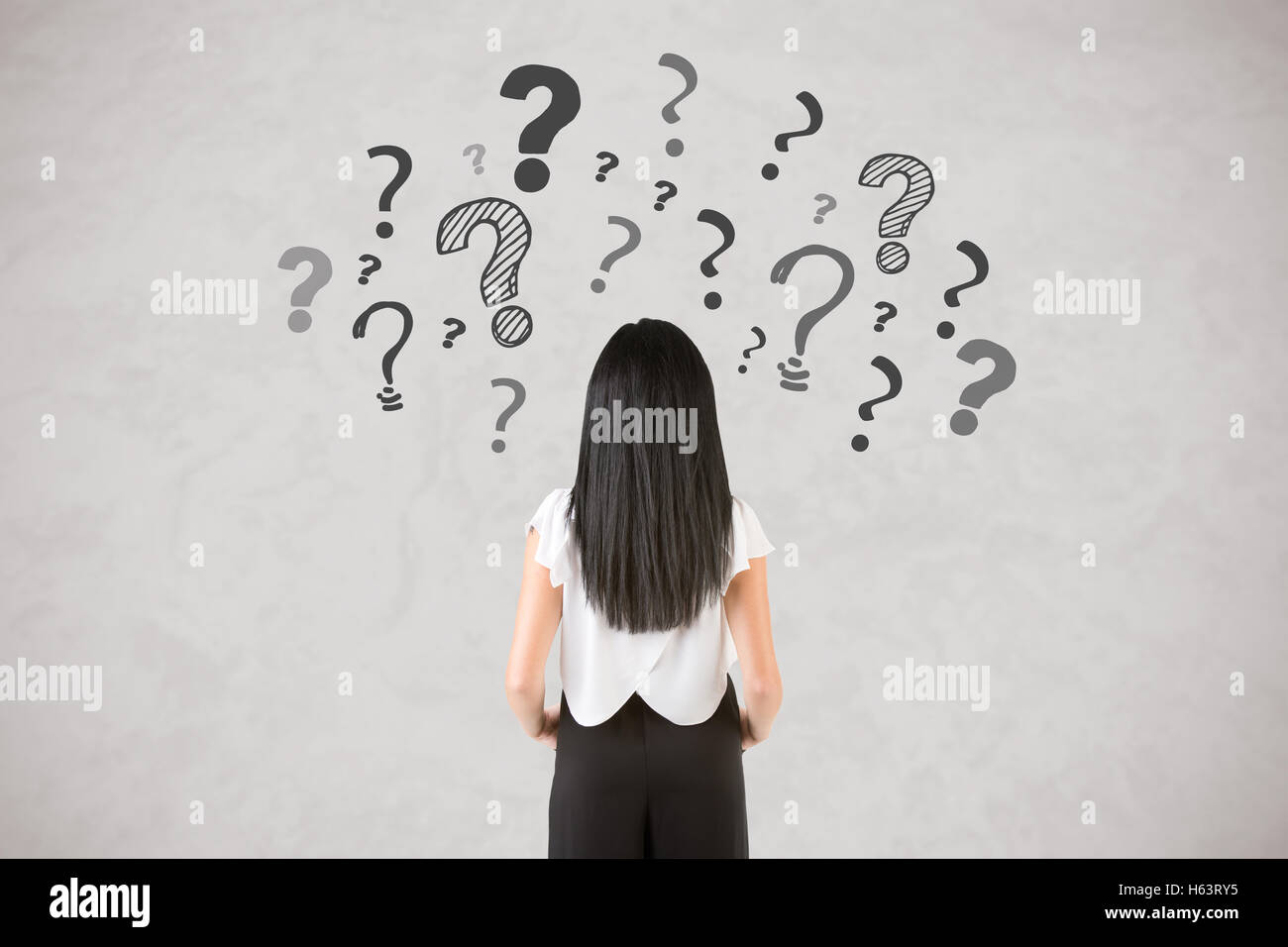 Backside of a businesswoman with question marks around her, isolated in white Stock Photo