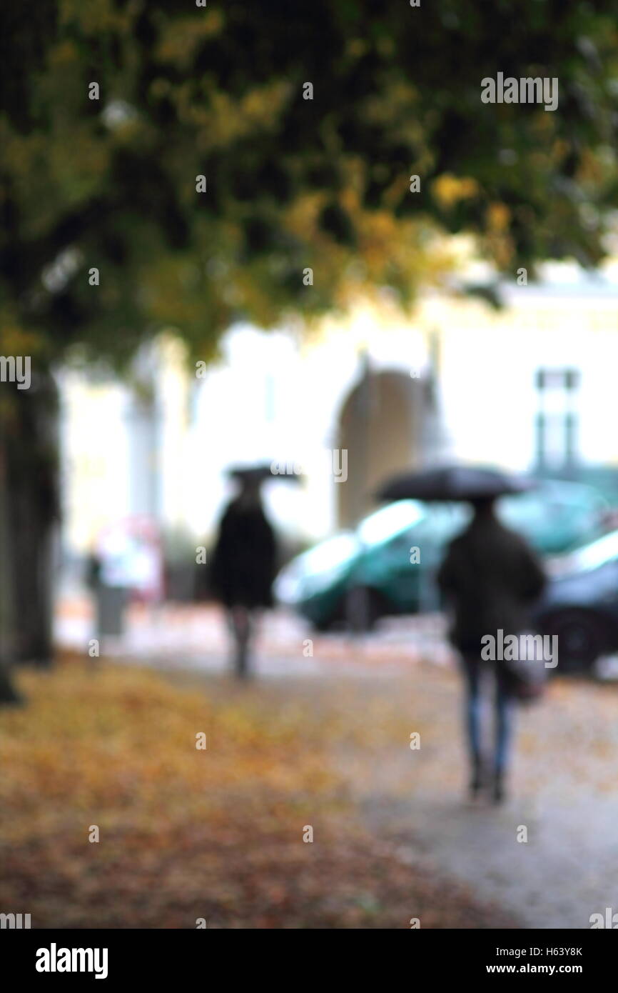 Blurred figures under black umbrella under fall rain. Stock Photo
