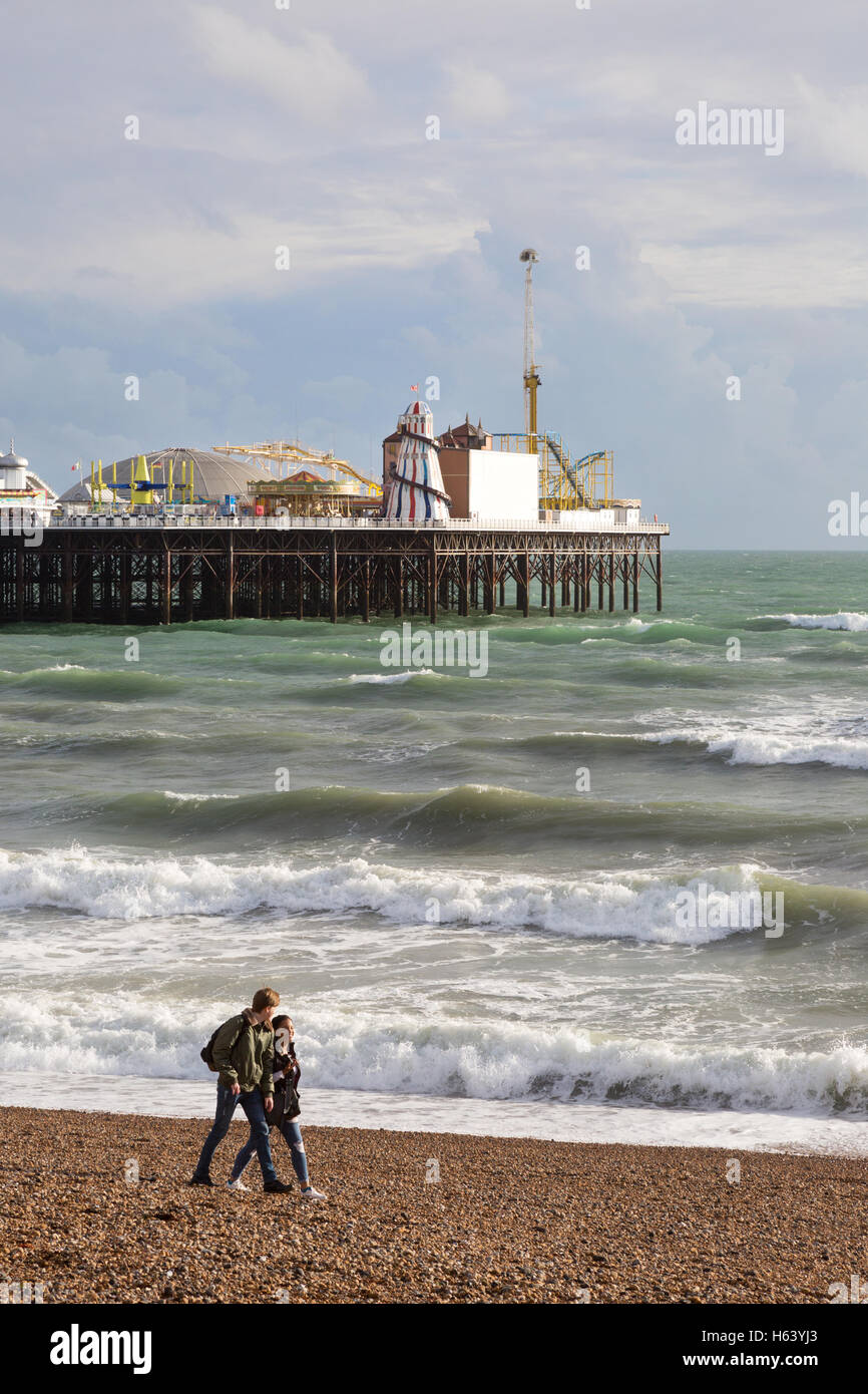 A couple walking on Brighton beach, Brighton Pier in the background, Brighton, East Sussex England UK Stock Photo