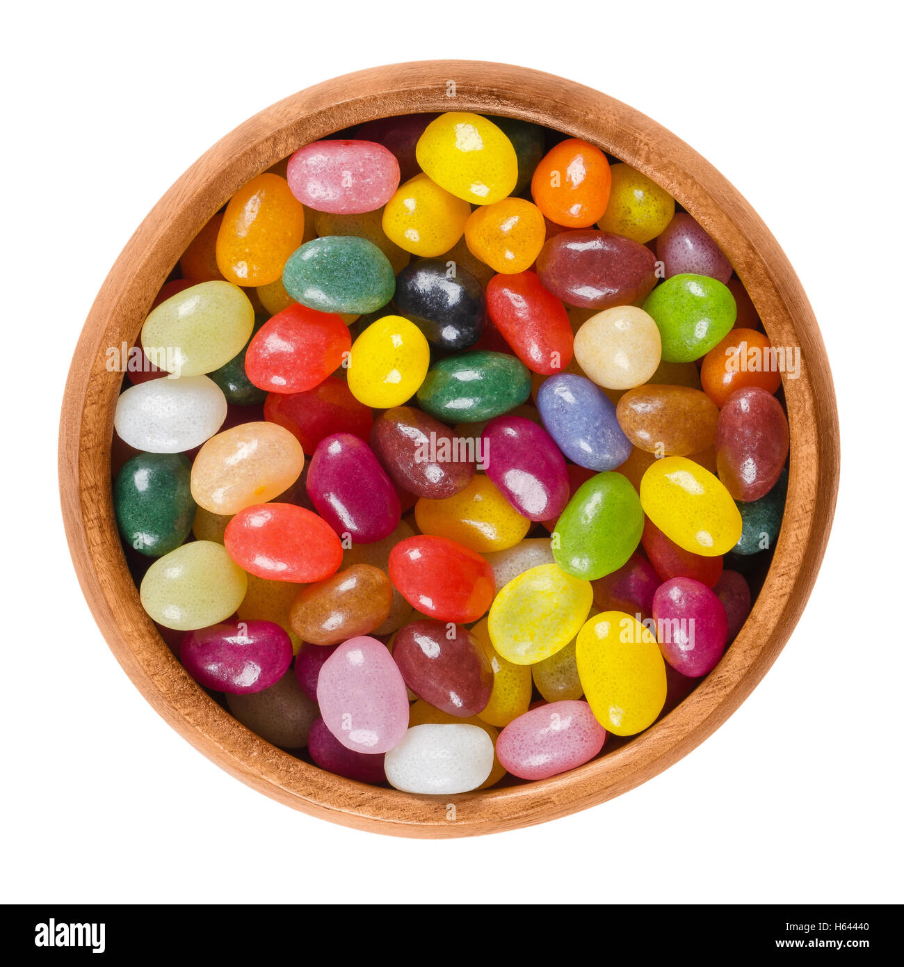 Jelly beans in wooden bowl on white background. Assorted small bean-shaped sugar candies in different colors with soft candy. Stock Photo