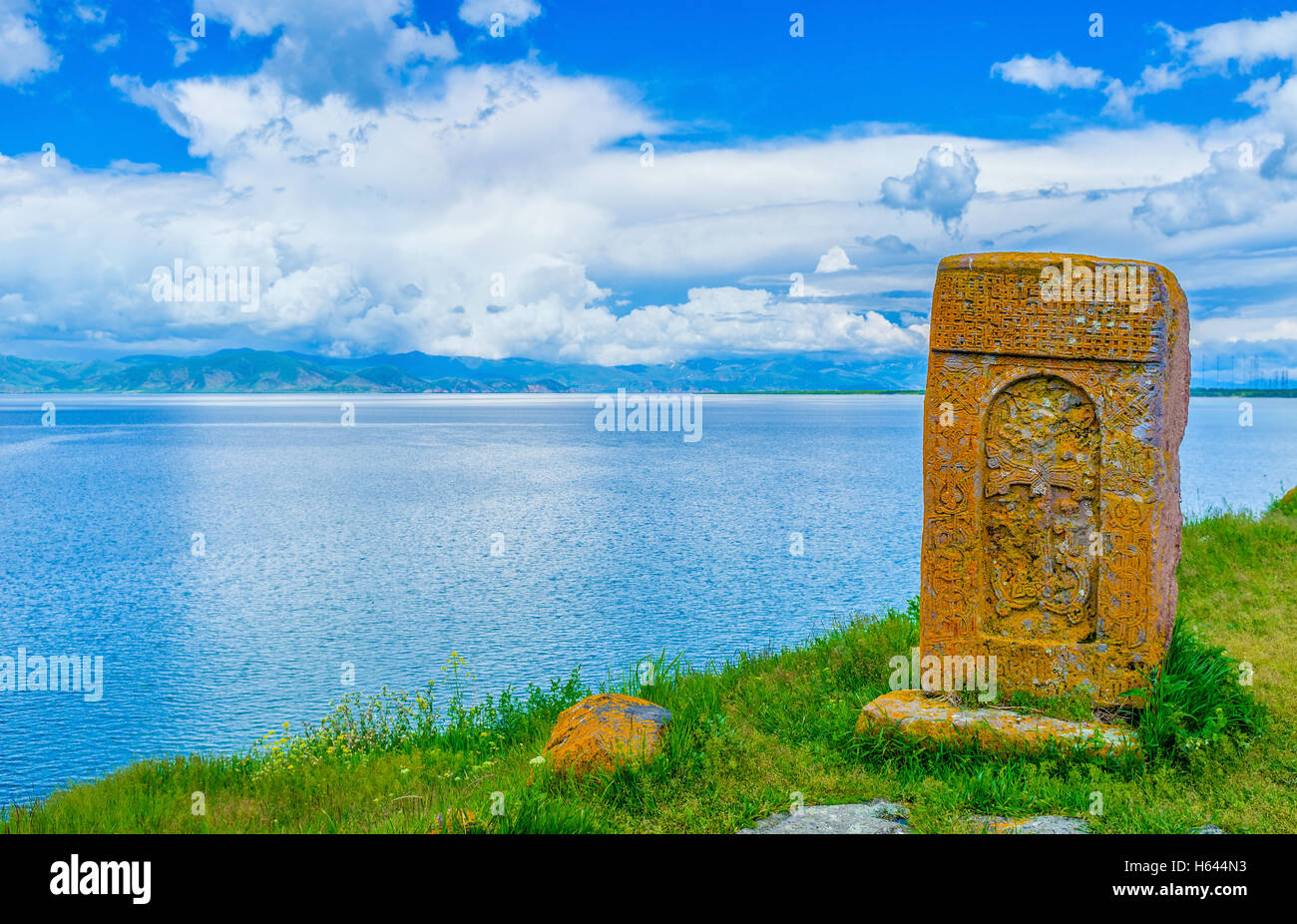 The orange khachkar, covered with lichen, located on the bank of Sevan Lake, on cemetery of Hayravank Monastery, Armenia. Stock Photo