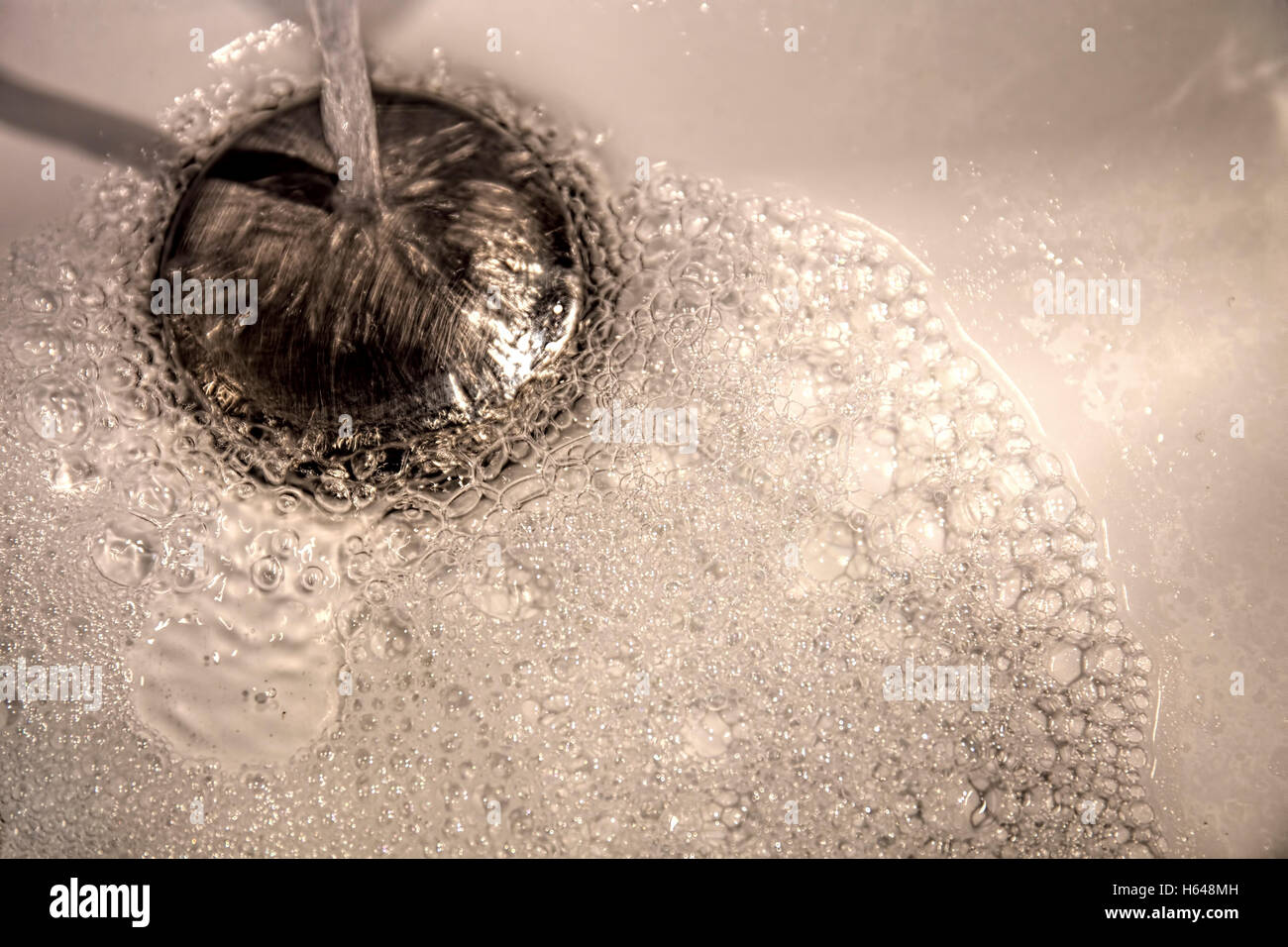 Running water pours into a wash basin with modern stainless steel sink plug fitting Stock Photo