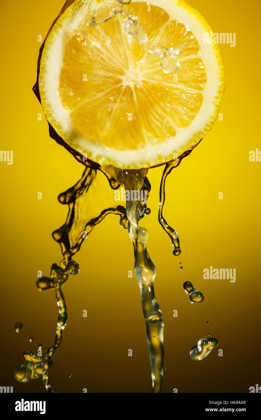 Lemon juice pouring down from half of  isolated on orange background Stock Photo