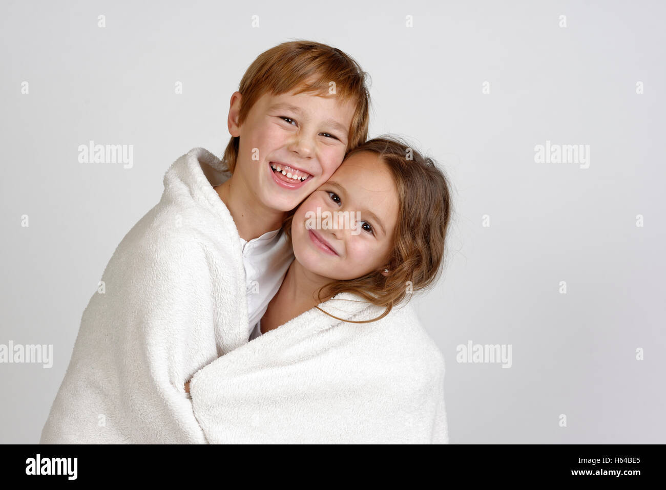 Portrait of laughing boy sharing blanket with his little sister Stock