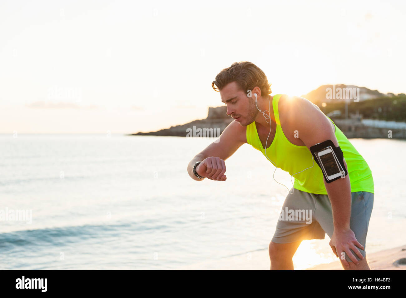 Spain, Mallorca, Jogger at the beach with headphones, looking on smartwatch Stock Photo