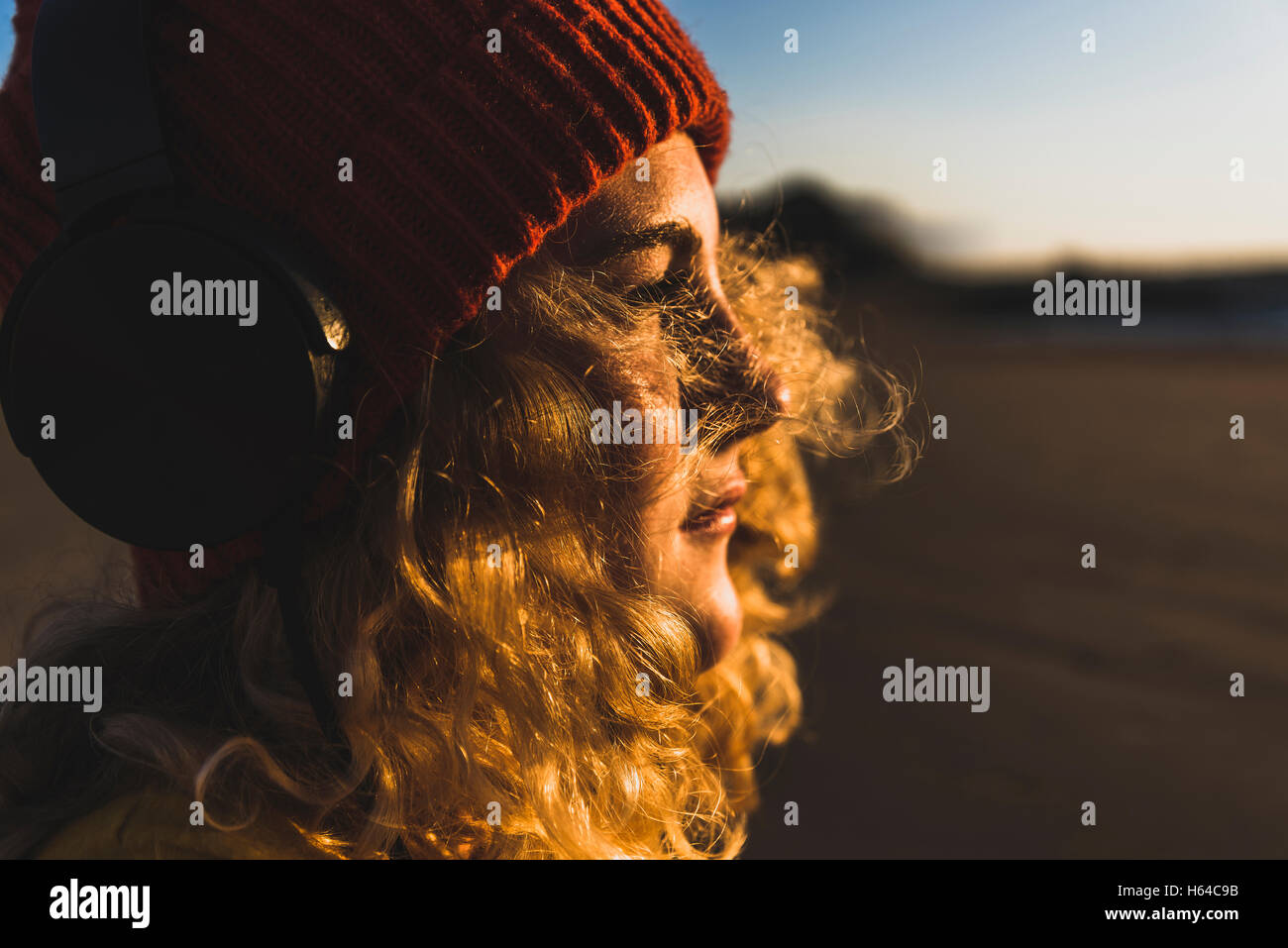 Teenage girl wearing beanie and headphones sitting on the beach Stock