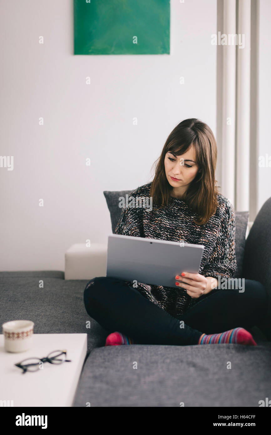 Young woman sitting on the couch using her tablet Stock Photo - Alamy