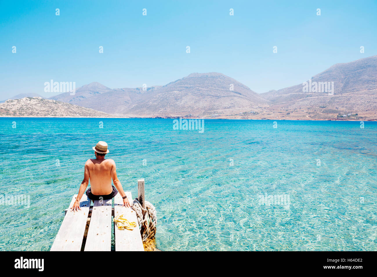 Greece, Cyclades islands, Amorgos, man sitting on the edge of a wooden pier, Nikouria island Stock Photo